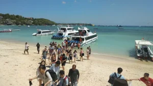 Passengers wading through shallow water to board a fast boat at Jungut Batu fast boat Beach, Nusa Lembongan, traditional beach embarkation.